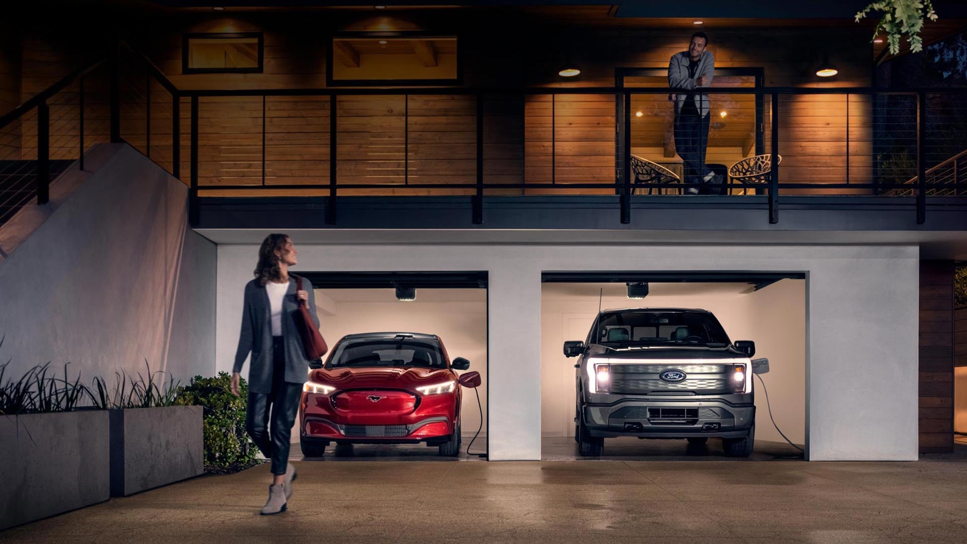 Woman walking out from home garage with a 2024 Mustang® Mach-E and Ford Lightning® truck in plugged-in and charging | Ames Ford in Ames IA