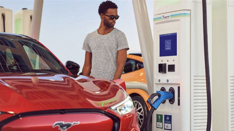 A man plugs in a Mustang Mach-E at a public charging station